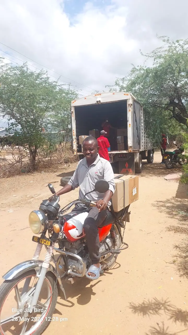 A driver on a motorbike loaded with boxes of books beside a delivery truck