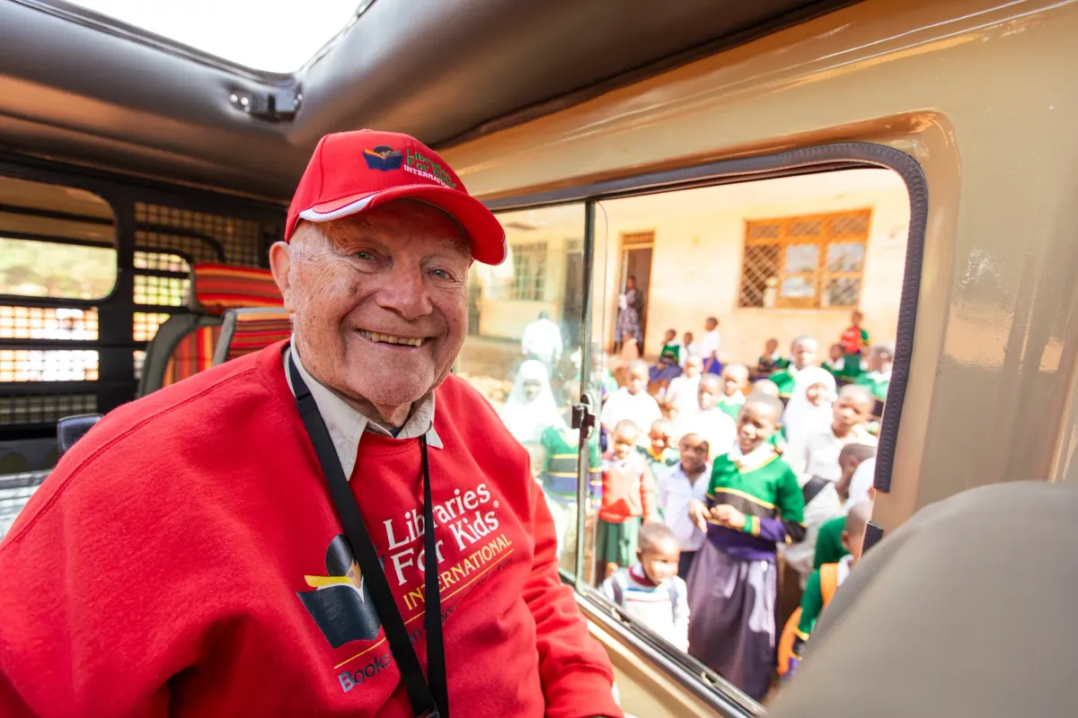 Coach Roy Austin smiling from a van window, schoolchildren gathered outside